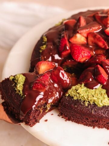 dubai chocolate strawberry cake on a cake stand with a spatula pulling out a slice