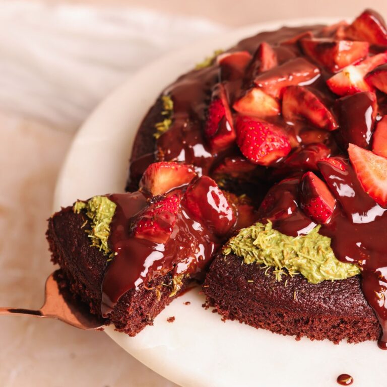 dubai chocolate strawberry cake on a cake stand with a spatula pulling out a slice