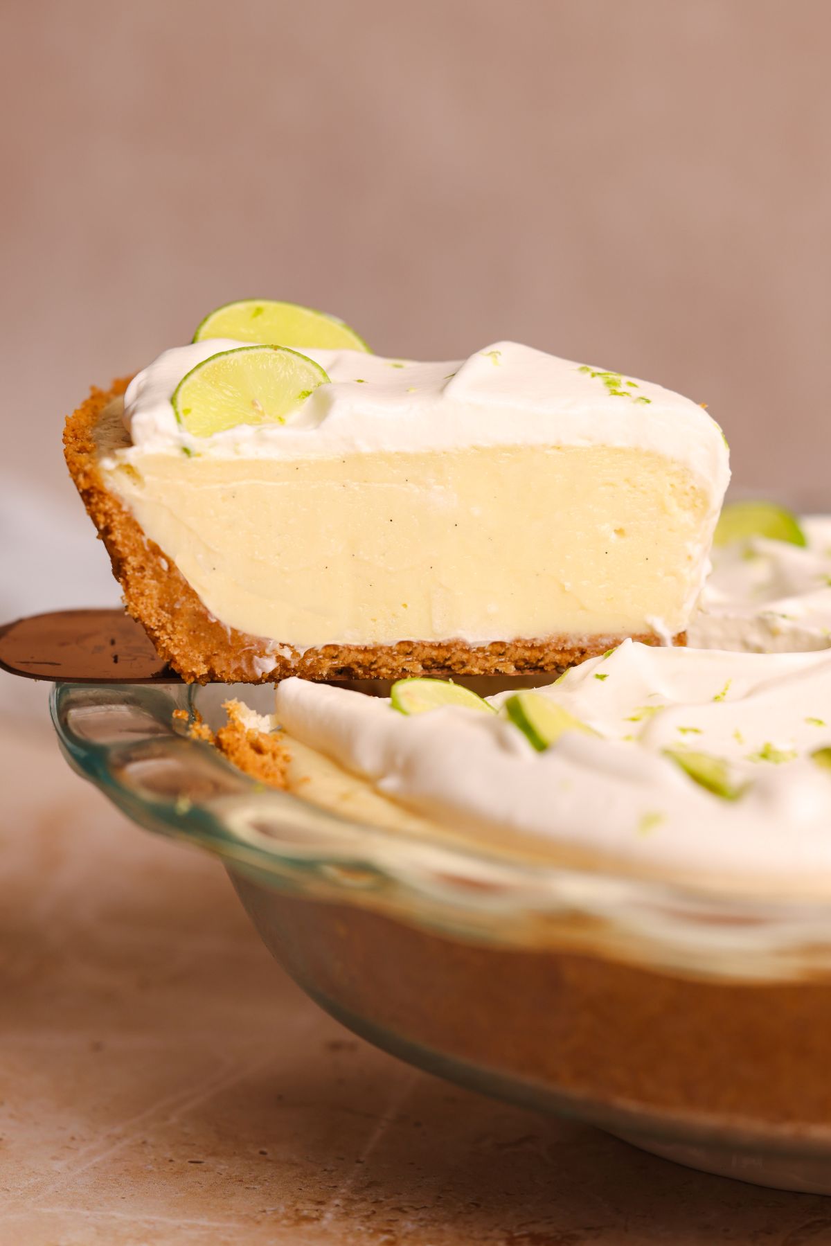a spatula pulling a slice of key lime pie out of the pie. the pie has a crispy crust and a creamy smooth filling