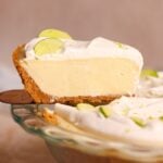 a spatula pulling a slice of key lime pie out of the pie. the pie has a crispy crust and a creamy smooth filling
