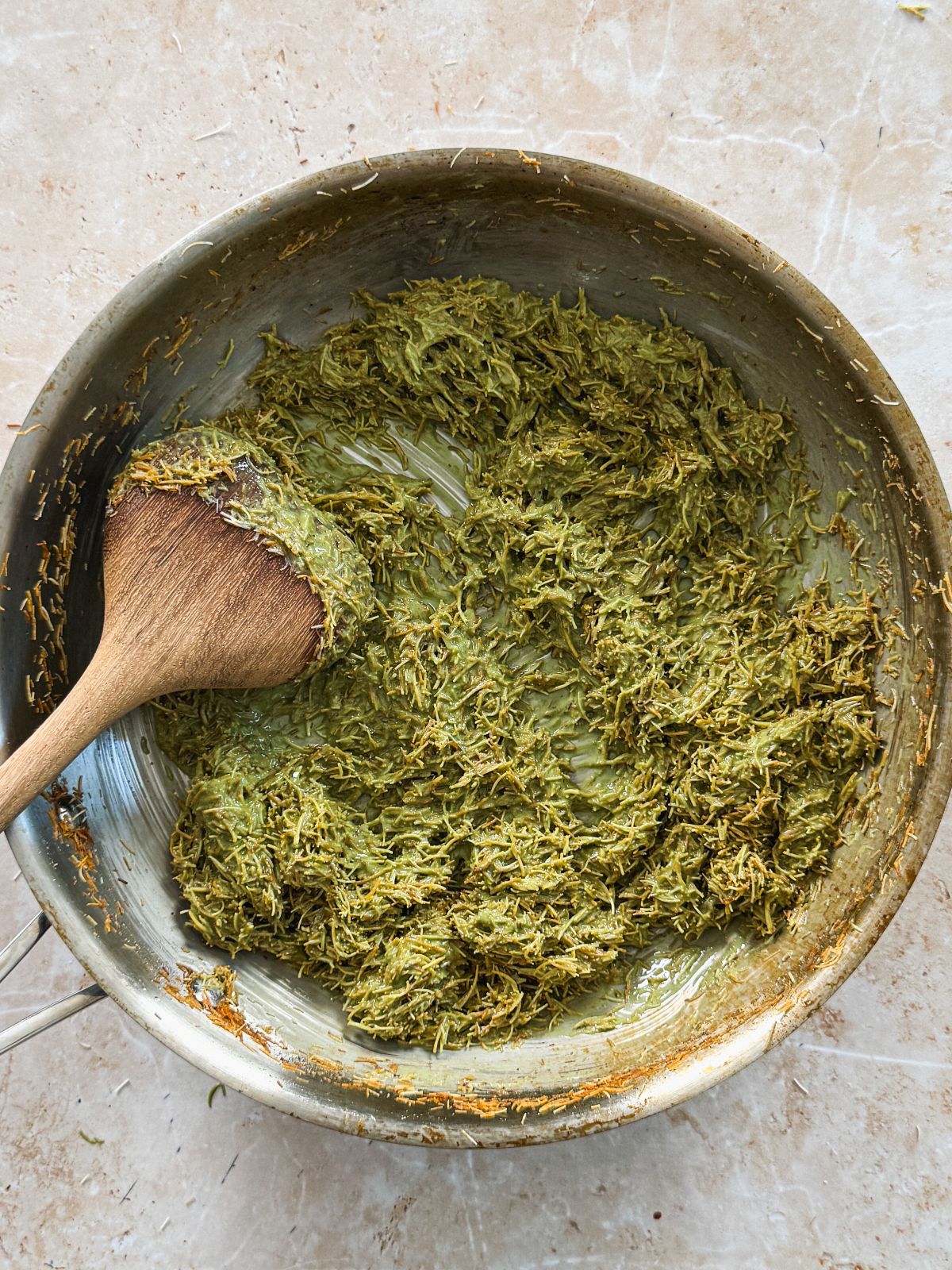 pistachio knafeh mixture in a stainless steel pan with a wooden spatula