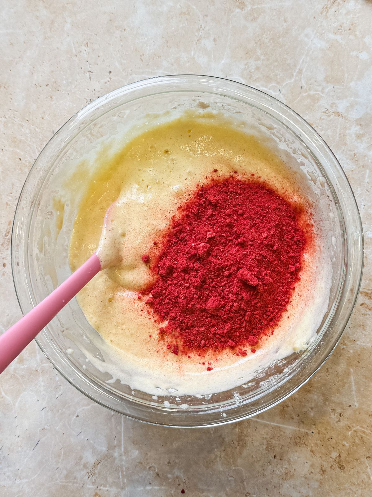 crushed freeze dried strawberries added on top of cake batter in a glass bowl