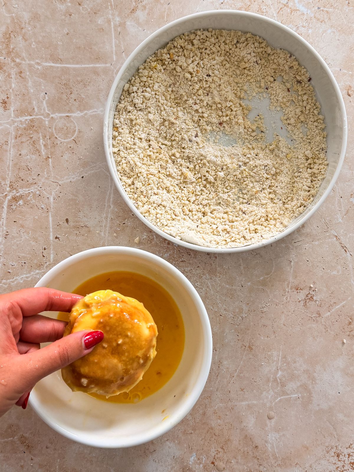 hand holding a bread pocket dipped in egg wash above a bowl with egg wash in it