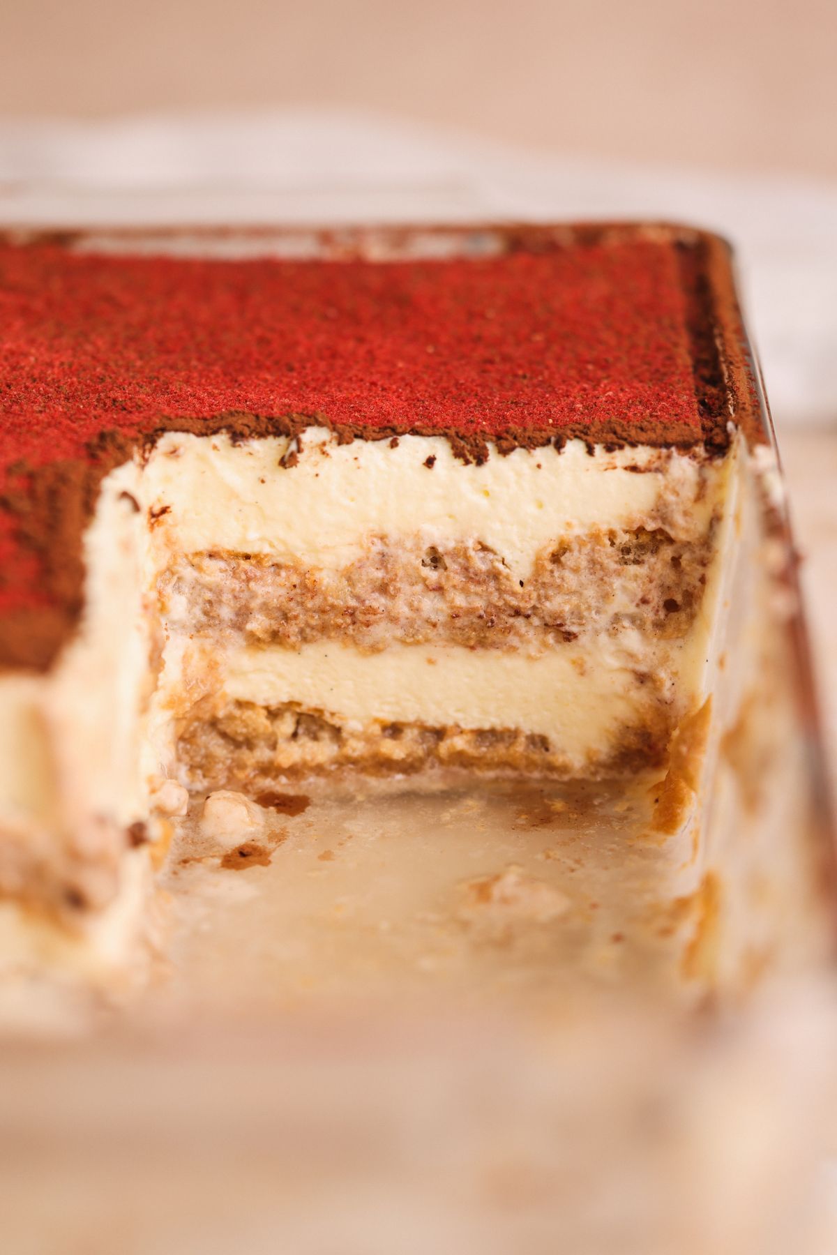 A close-up view of a rectangular dish of chai tiramisu with a large slice removed, revealing creamy layers of mascarpone cheese, chai-soaked ladyfingers, and a dusting of cocoa powder on top.