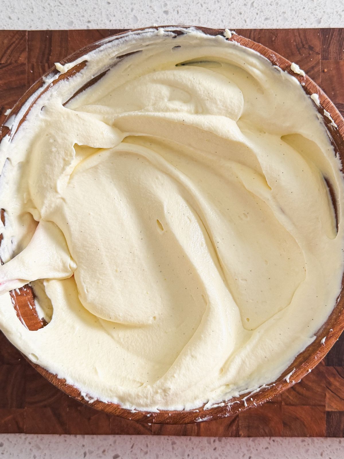 A round wooden bowl filled with smooth, creamy, pale yellow mascarpone cream is placed on a wooden surface.
