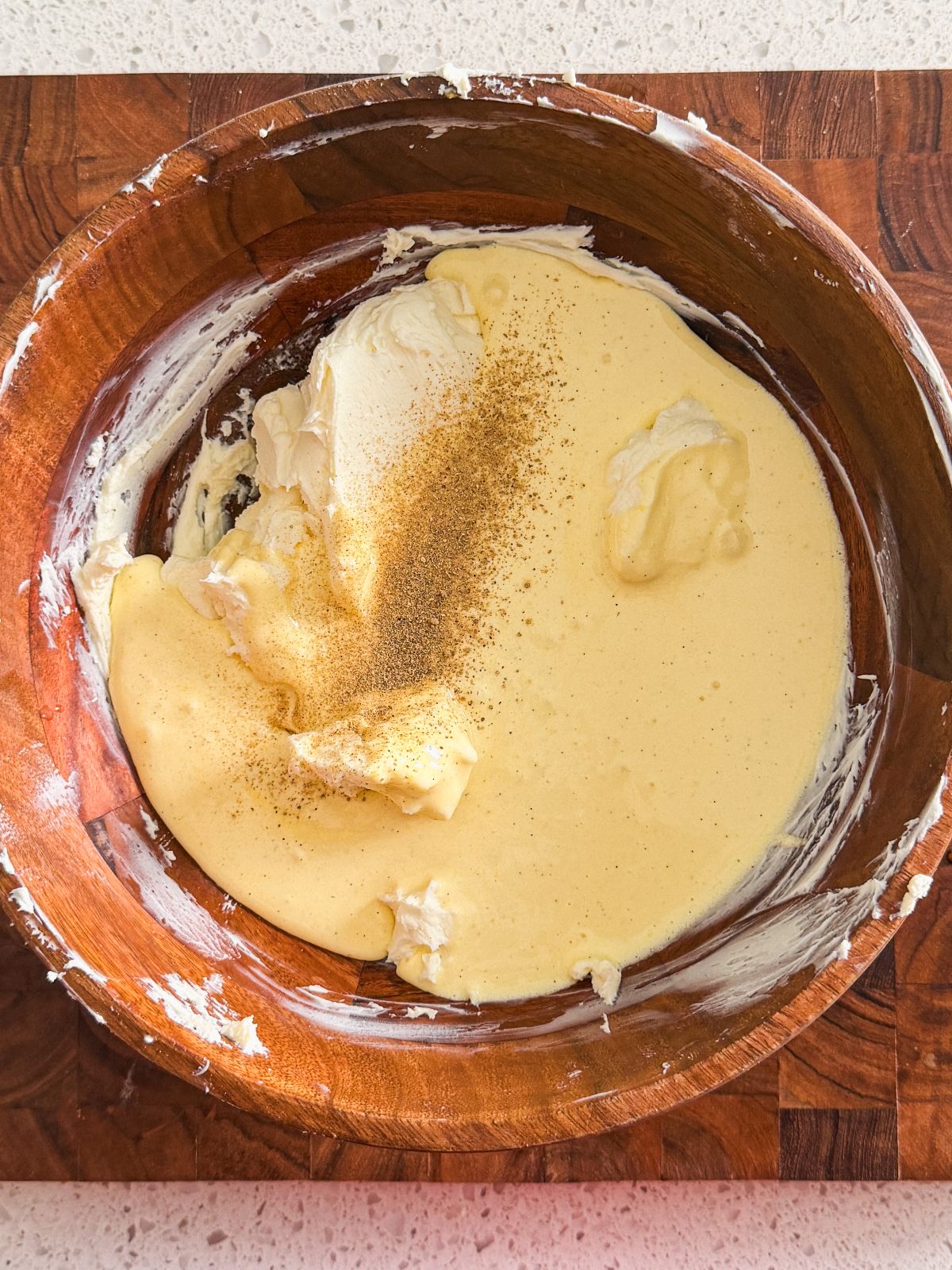eggs and sugar poured on top of mascarpone cheese and a sprinkle of caramom in a wooden bowl on a wooden board