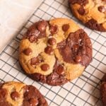 A large, round brookie cookie with brownie and cookie dough swirled together, topped with chocolate chips and a sprinkle of sea salt, cooling on a wire rack.