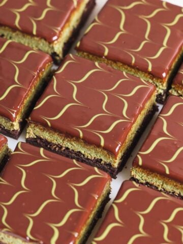 Nine square dubai chocolate brownies with glossy chocolate ganache, each topped with a green wavy line pattern. The pastries have visible layers including a light green and a dark brown layer.