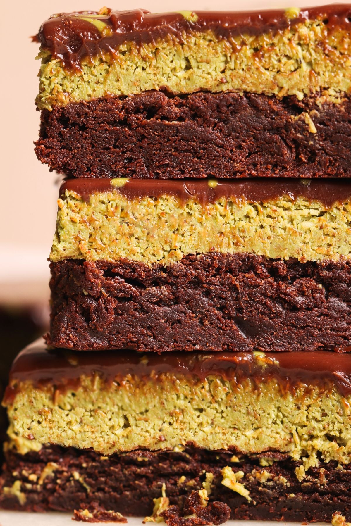 A close-up of three stacked dubai chocolate brownies with a dense, dark chocolate brownie base, a thick pistachio knafeh layer, and a glossy chocolate topping. The bars have a rich, textured appearance.