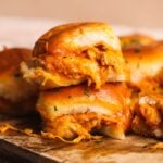 A close-up of cheesy, saucy chipotle chicken sliders stacked on a wooden board, with golden, soft buns and shredded chicken filling visible.