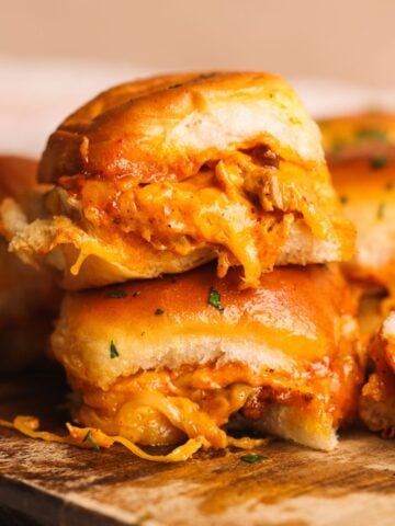 A close-up of cheesy, saucy chipotle chicken sliders stacked on a wooden board, with golden, soft buns and shredded chicken filling visible.