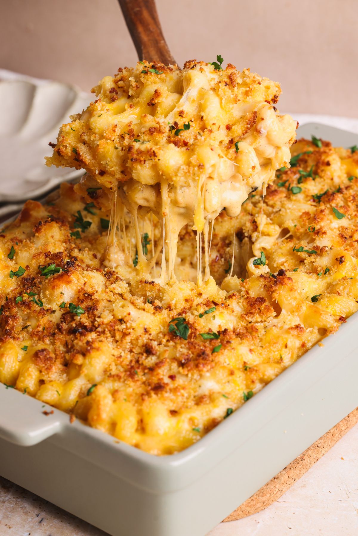 A close-up of creamy baked macaroni and cheese with a golden breadcrumb topping being scooped from a casserole dish, showing gooey melted cheese stretching from the serving.