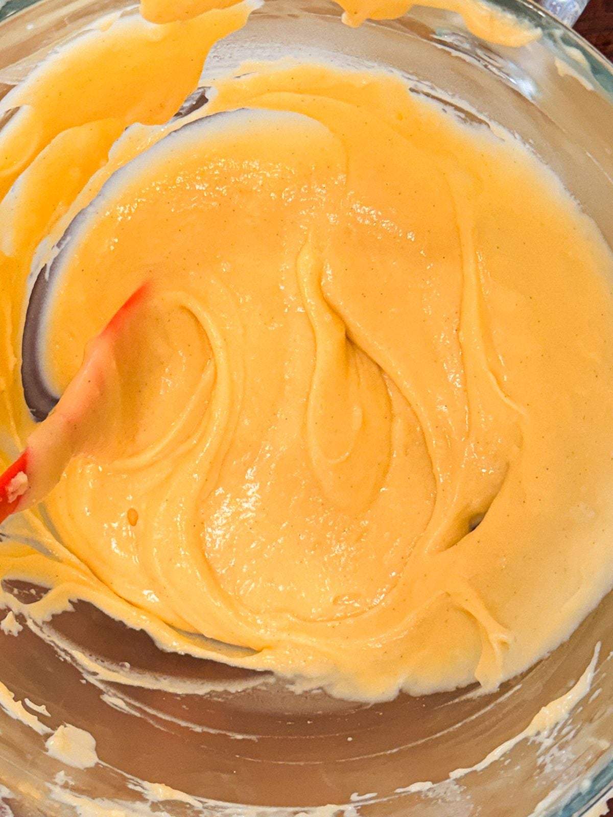 Thick yellow choux pastry in a glass bowl with a red spatula.