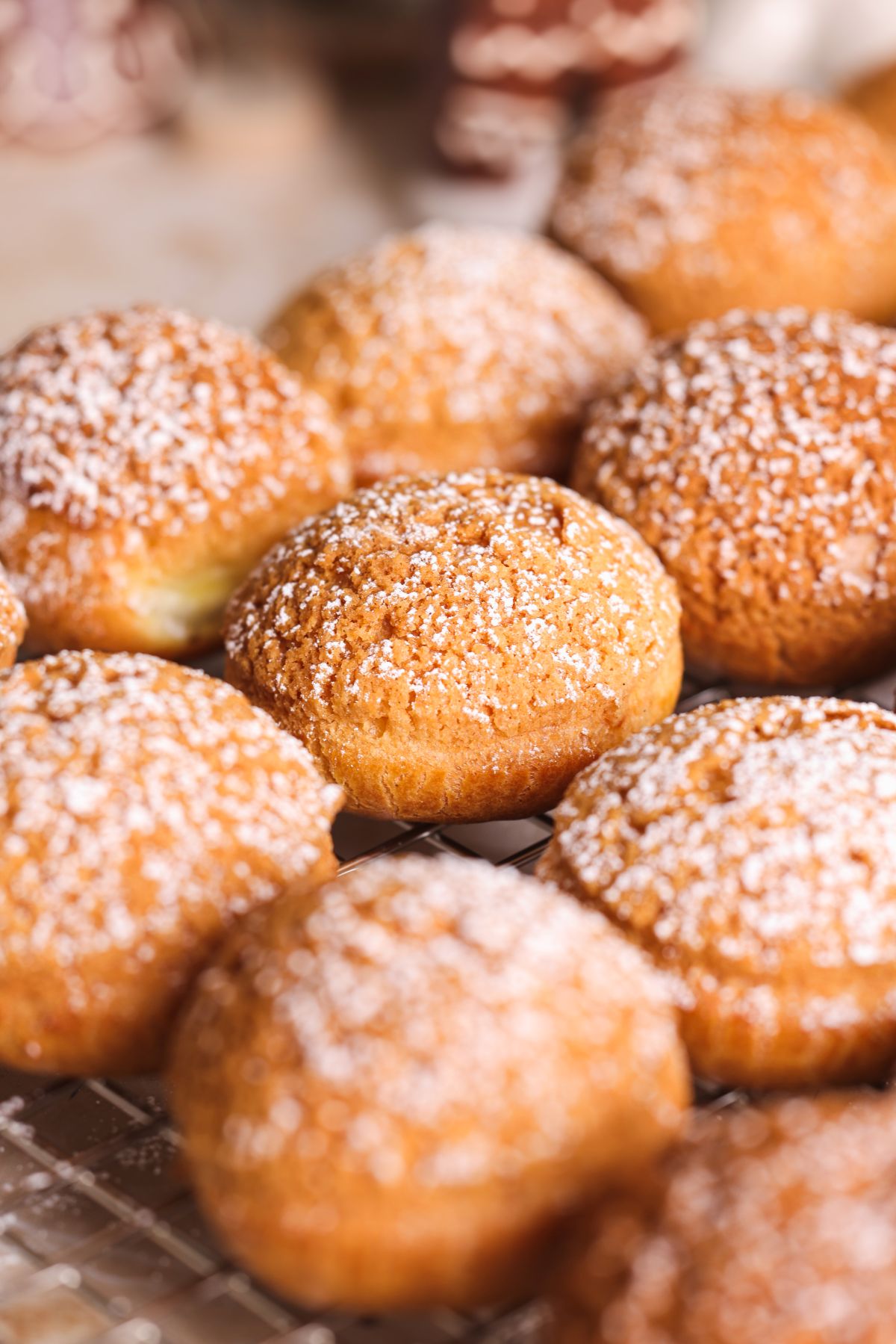 A close-up of several round, golden-brown cream puffs topped with powdered sugar, arranged on a cooling rack.