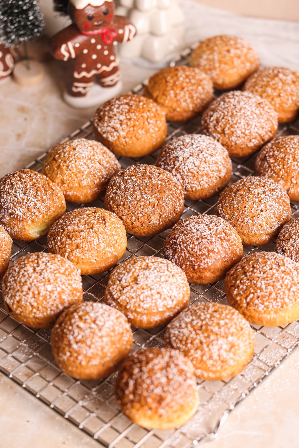 A cooling rack filled with round cream puffs dusted with powdered sugar. In the background, there are festive decorations, including a gingerbread figurine and a small Christmas tree.