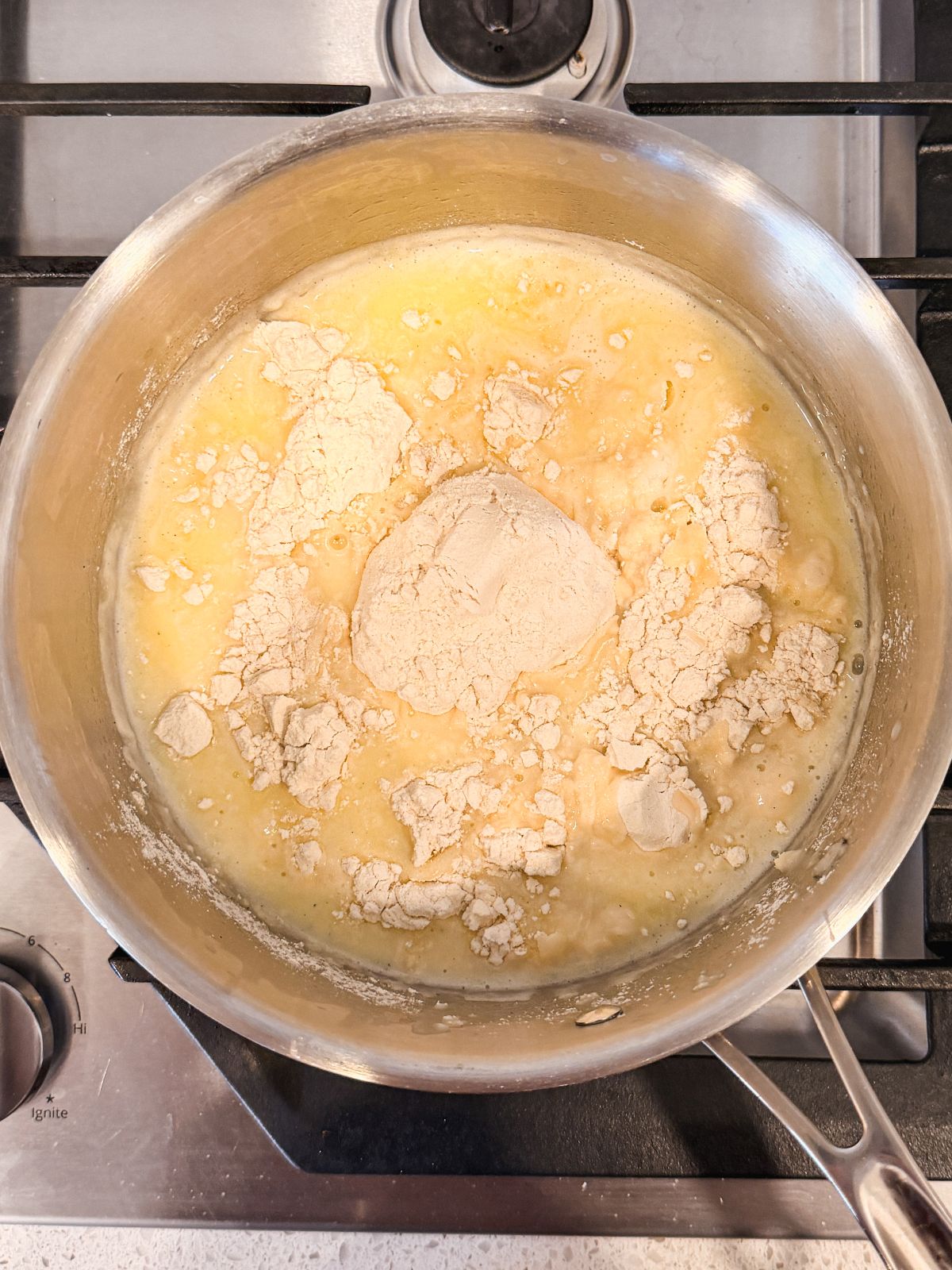 A saucepan on a stove contains melted butter with a mound of flour on top, starting to be mixed together for a roux.