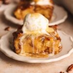 A slice of sticky toffee bread pudding topped with a scoop of vanilla ice cream and drizzled with toffee sauce, served on a small white plate.
