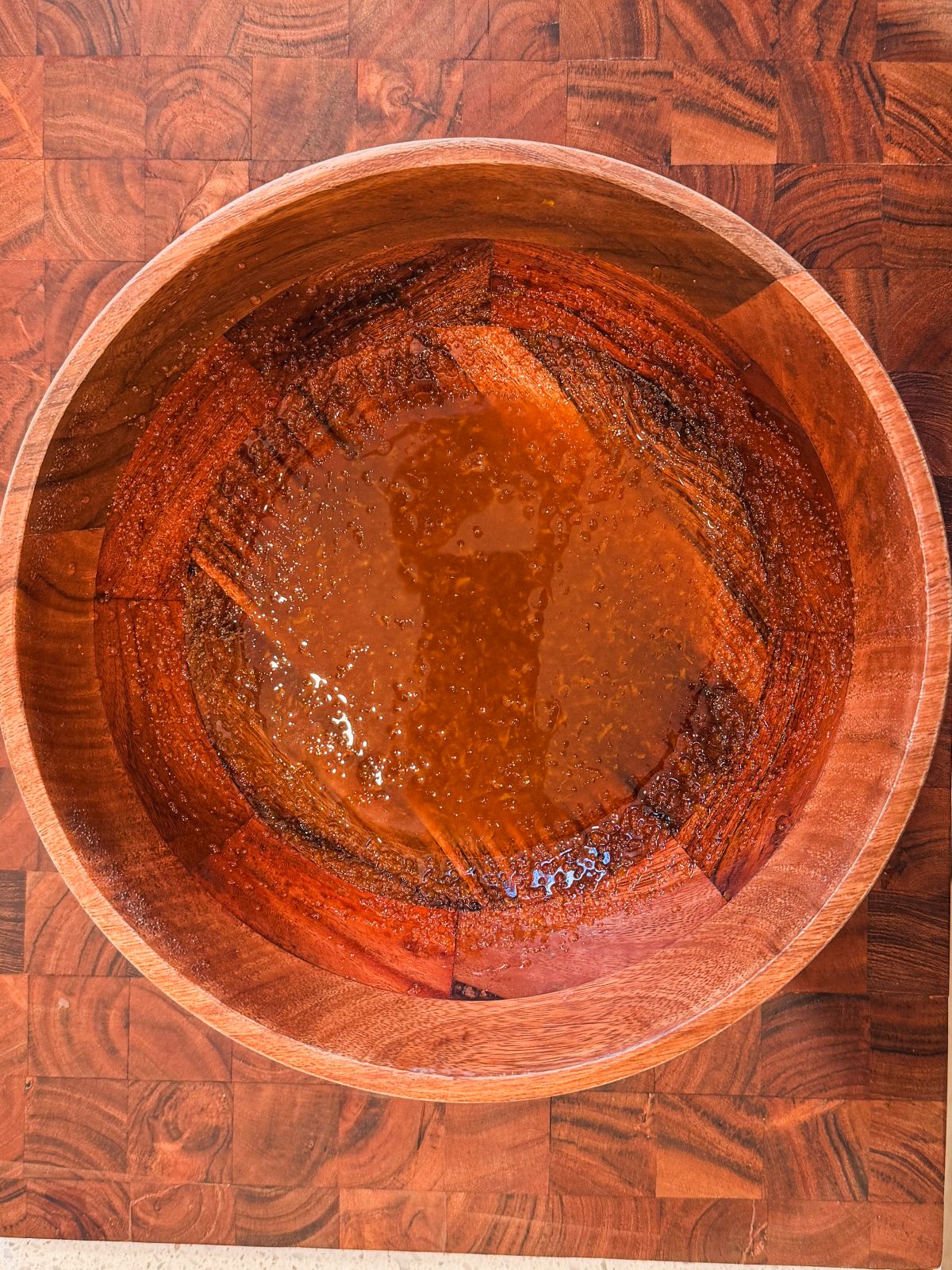 A large wooden bowl with oil, sugar and zest , sitting on a wooden surface.