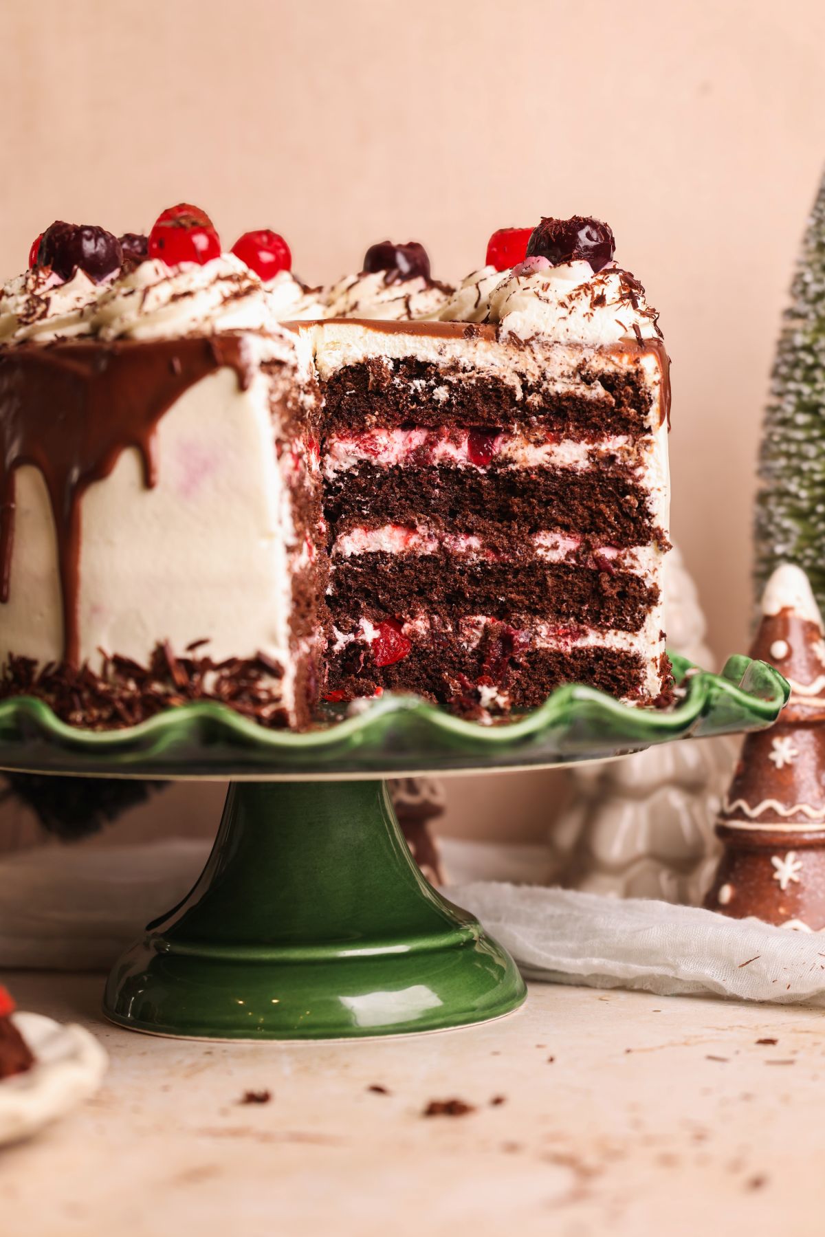 A Black Forest cake with chocolate sponge layers, whipped cream, and cherries is displayed on a green cake stand. A large slice has been cut, revealing the cakes rich, layered interior.