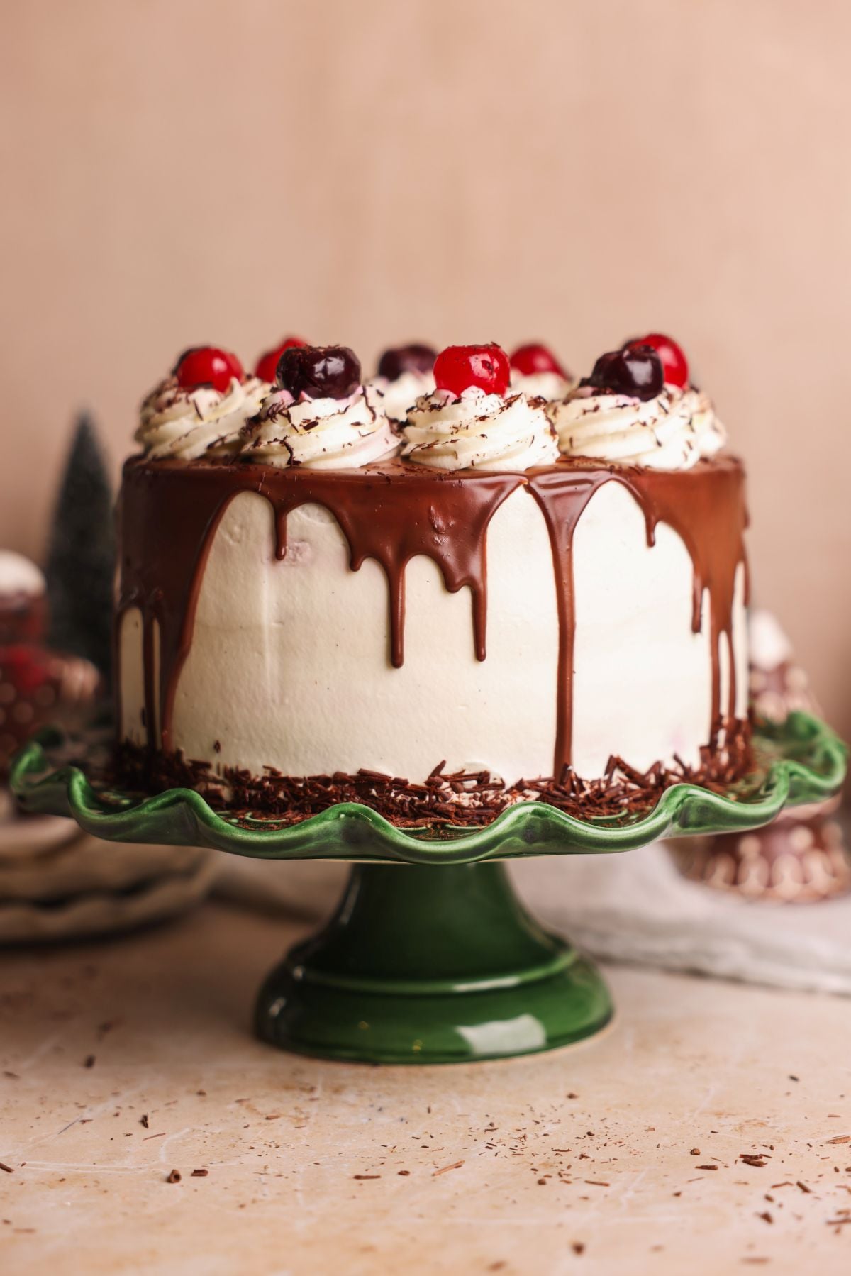 A chocolate-dripped black forest cake with whipped cream, , cherries, and chocolate shavings, displayed on a green cake stand.