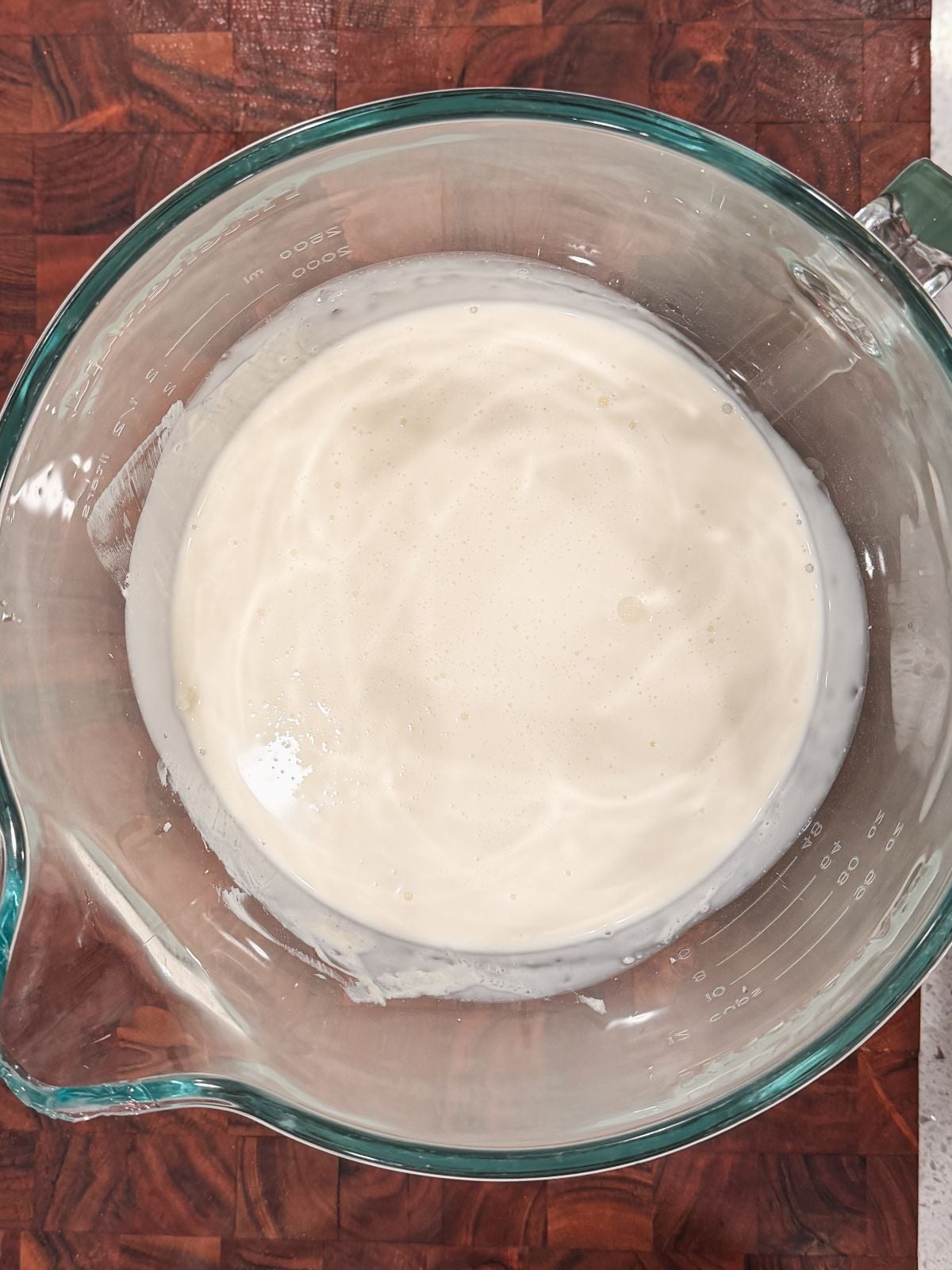 A glass mixing bowl filled with a creamy white batter or liquid sits on a wooden countertop.