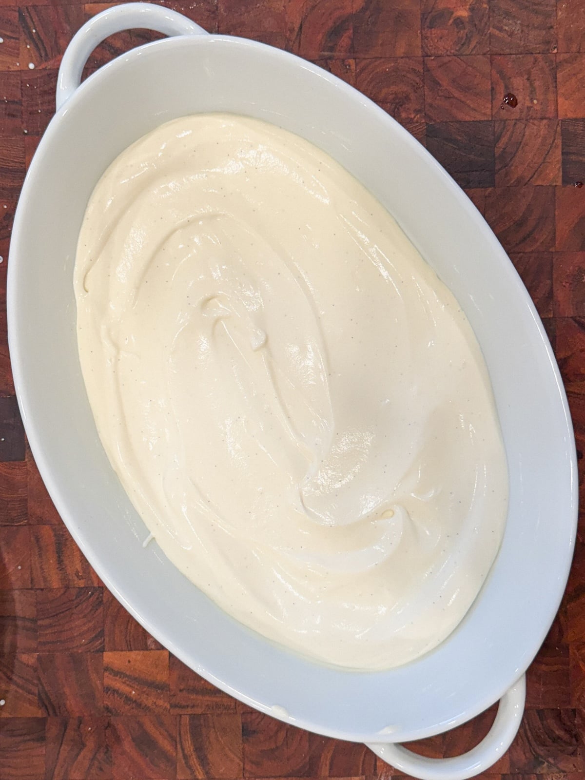 An oval white ceramic dish filled with smooth, creamy vanilla pudding sits on a wooden surface.