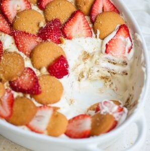A close-up of a dessert dish with layers of vanilla wafers, fresh strawberry slices, and creamy pudding, shown partially served to reveal the inside layers.