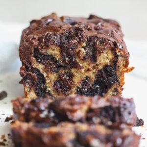 A close-up of a sliced loaf of chocolate brownie swirl banana bread, showing moist, marbled layers of banana bread and melted chocolate. The loaf is set on a light background, and the texture appears rich and gooey.