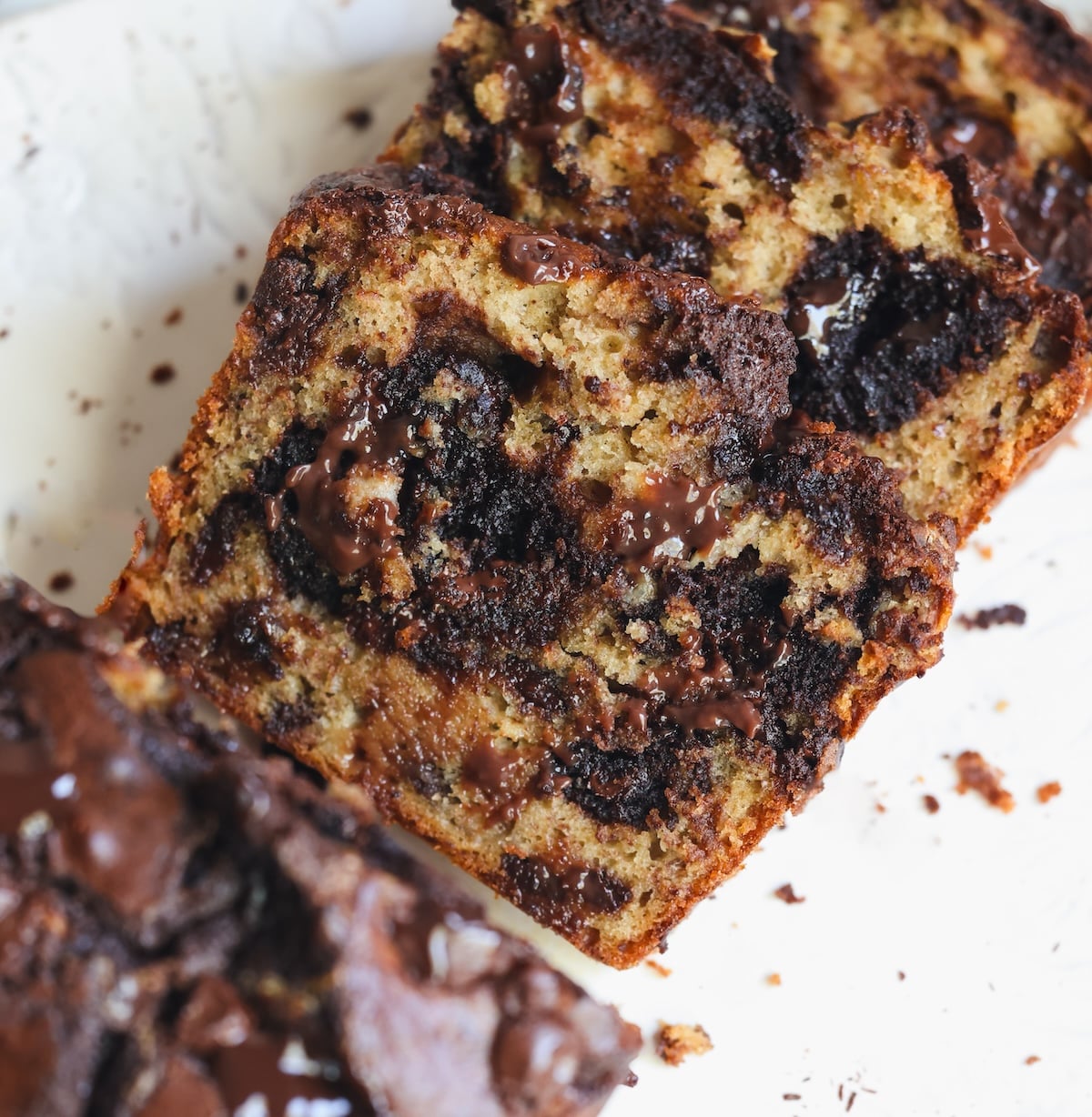 Sliced brownie chocolate marble banana bread with melted chocolate swirls, displayed on a white surface with crumbs around the slices.