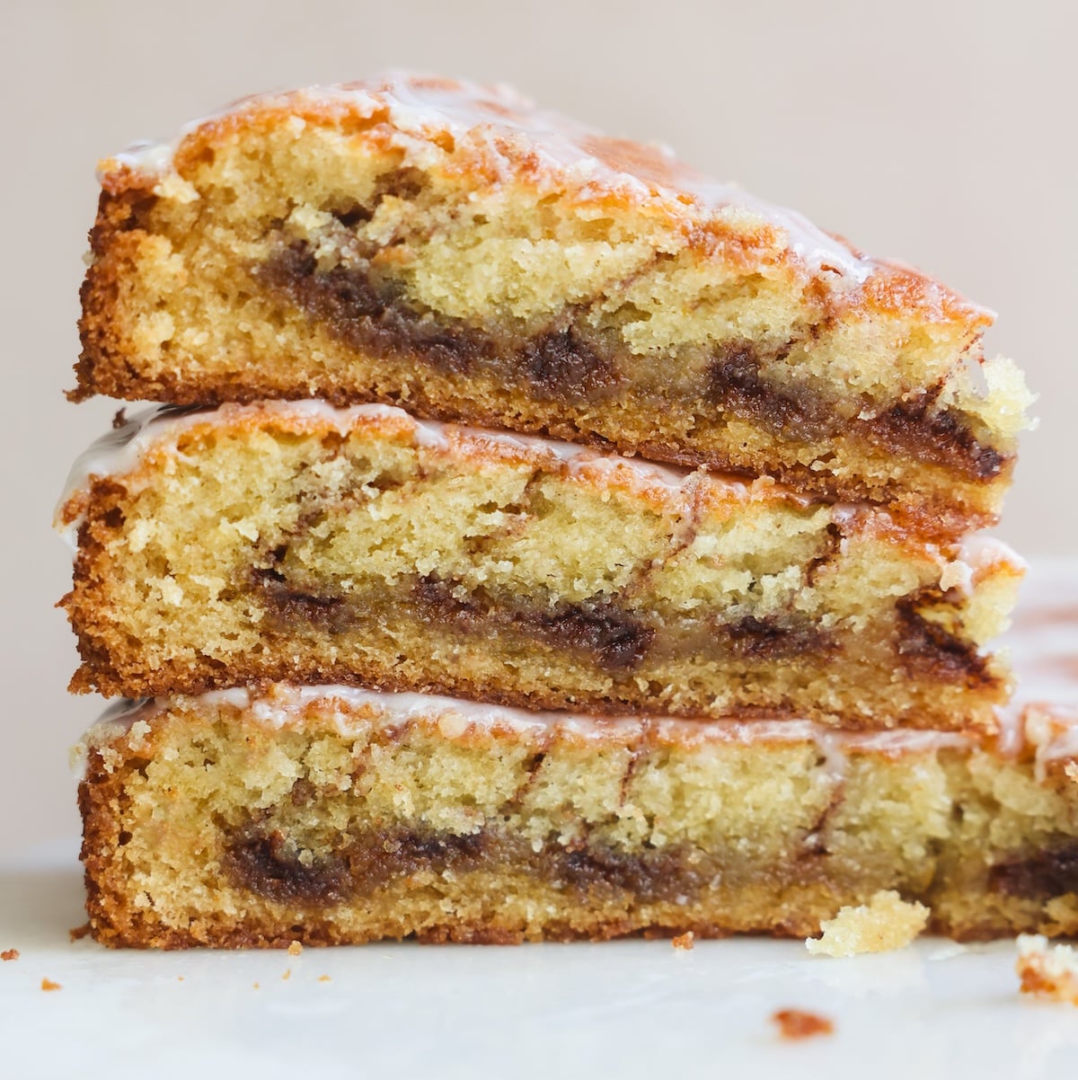 Three slices of cinnamon roll stacked on each other, showing a cinnamon swirl layer inside and a light glaze drizzled on top. The cake appears moist and golden with a tender crumb.