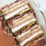 Three slices of layered tiramisu ice cream cake with visible layers of cream, chocolate, and espresso-soaked ladyfingers, placed on a white plate with some cocoa powder on the side.