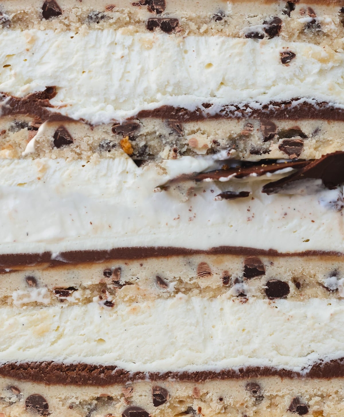 Close-up of a layered dessert with chocolate chip cookie dough, vanilla ice cream, and thin chocolate layers. The texture of the cookie dough and creamy filling are visible.