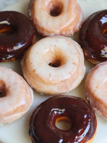 A plate of assorted donuts topped with chocolate glaze and white sugar glaze, arranged closely together on a round, white surface.