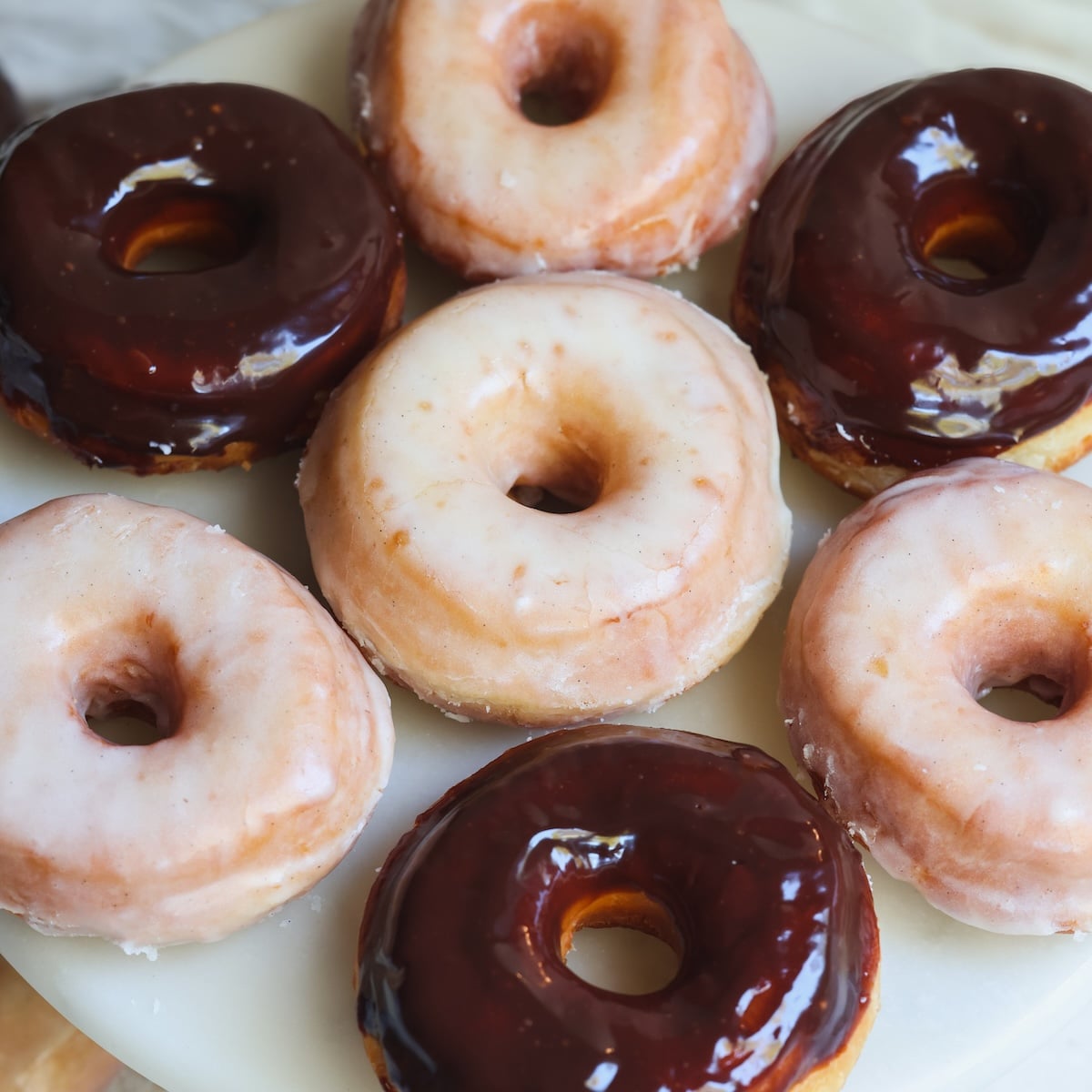 A plate of assorted donuts topped with chocolate glaze and white sugar glaze, arranged closely together on a round, white surface.