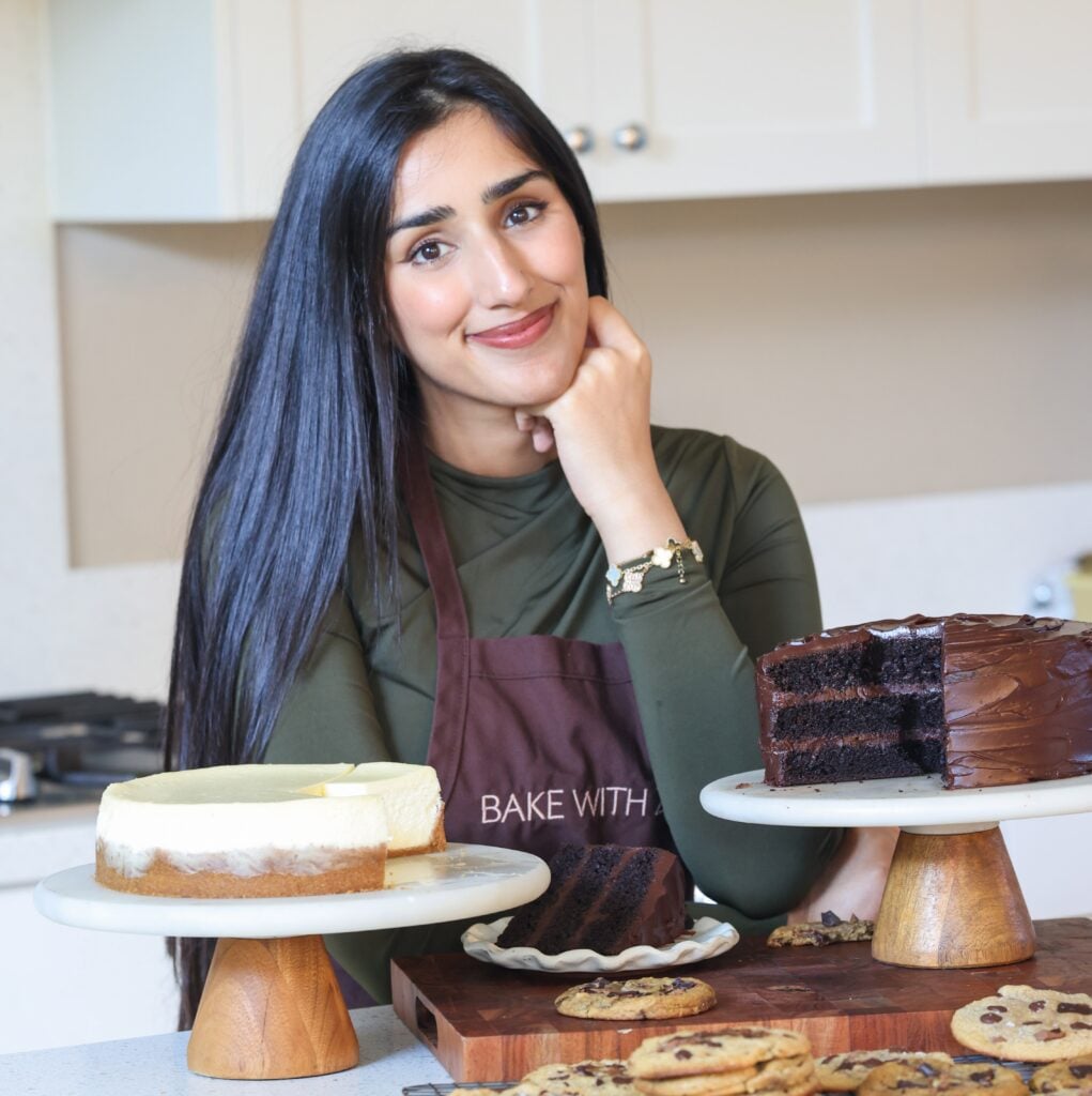 picture of zoha standing in front of a counter with a chocolate cake, cheesecake and cookies