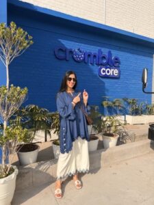 Zoha standing in front of a blue wall that has the crumble cookie logo on it