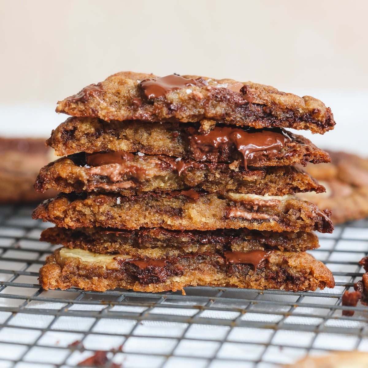 A stack of gooey banana bread chocolate chip cookies is cut in half, with melted chocolate oozing out, sitting on a cooling rack.