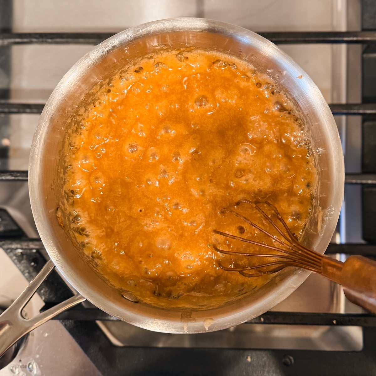 A saucepan of butterscotch bubbling on a stove, with a whisk stirring the mixture.