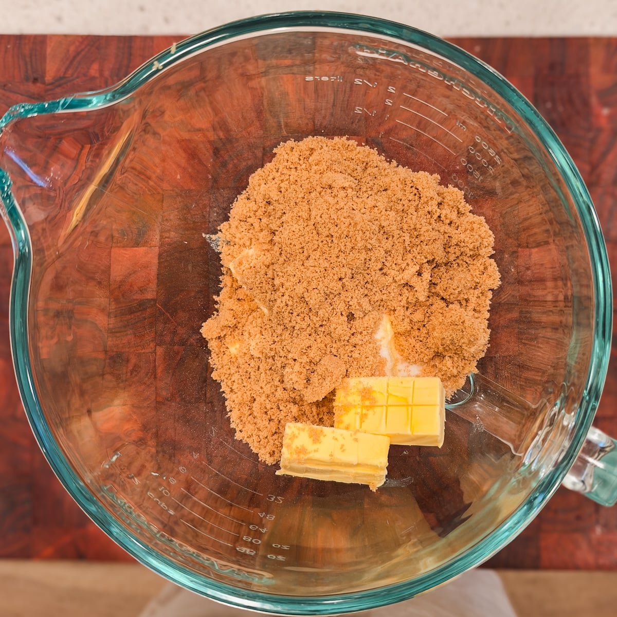 A glass mixing bowl containing a pile of brown sugar, white sugar and butter