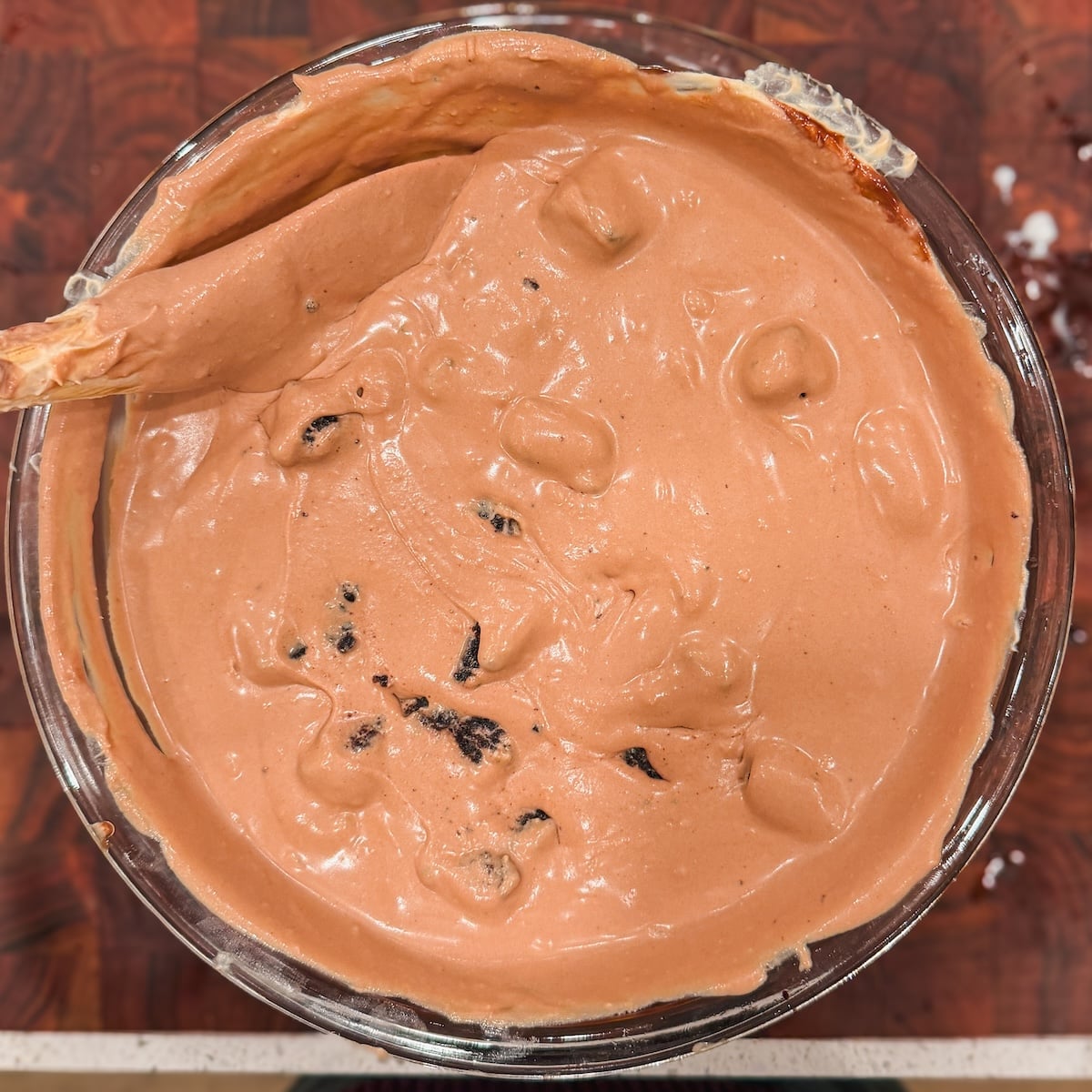 A glass bowl filled with creamy chocolate ice cream mixed with brownie chunks, with a wooden spoon resting on the edge.