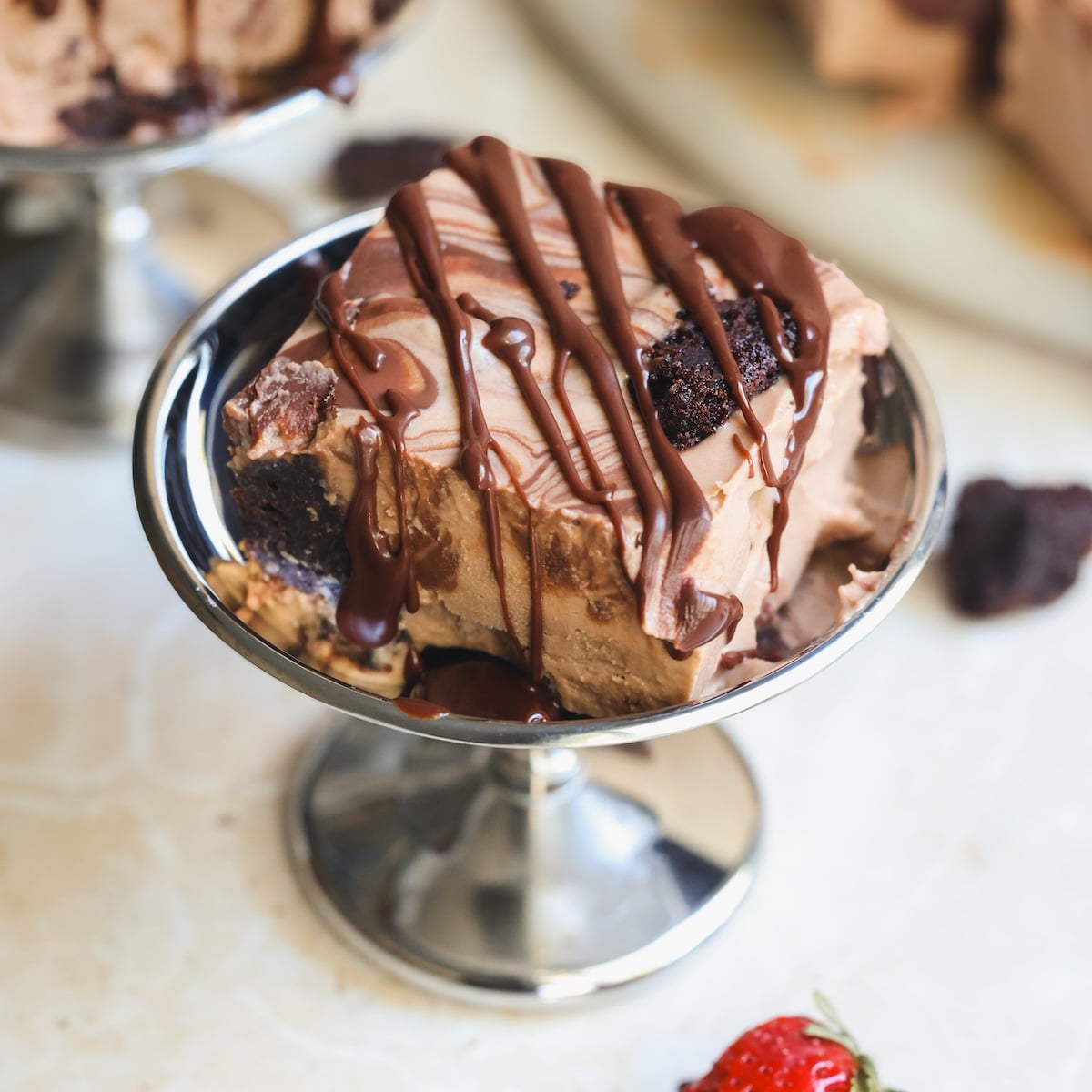 A square of chocolate brownie ice cream drizzled with chocolate sauce in a small metal pedestal dish.