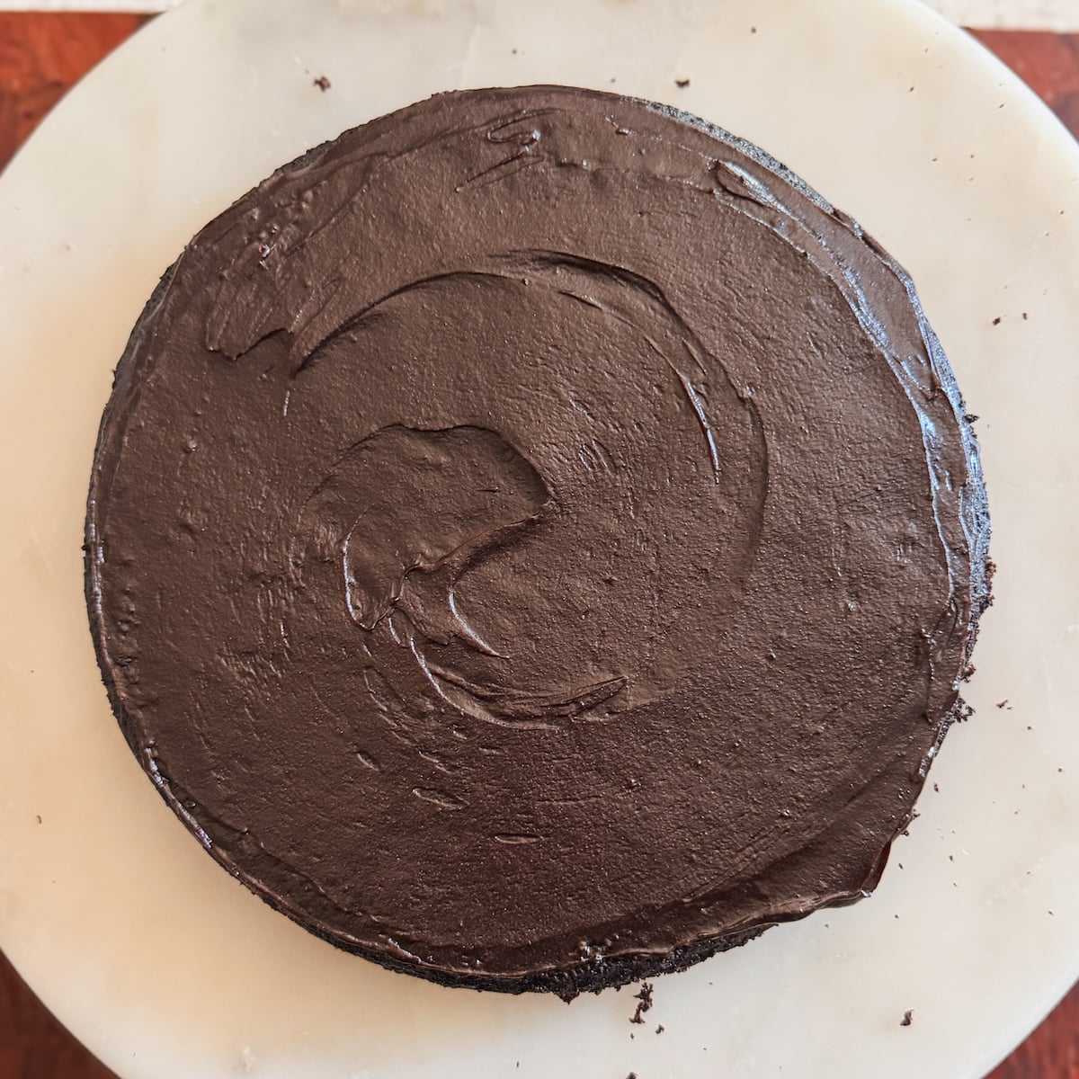 A round chocolate cake with smooth, chocolate fudge frosting sits on a white marble surface.