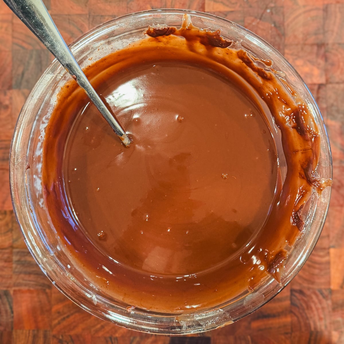 A glass bowl of ganache with a metal spoon inside.