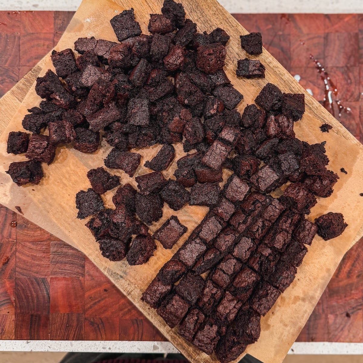A wooden cutting board covered in small cubes of chocolate brownie.
