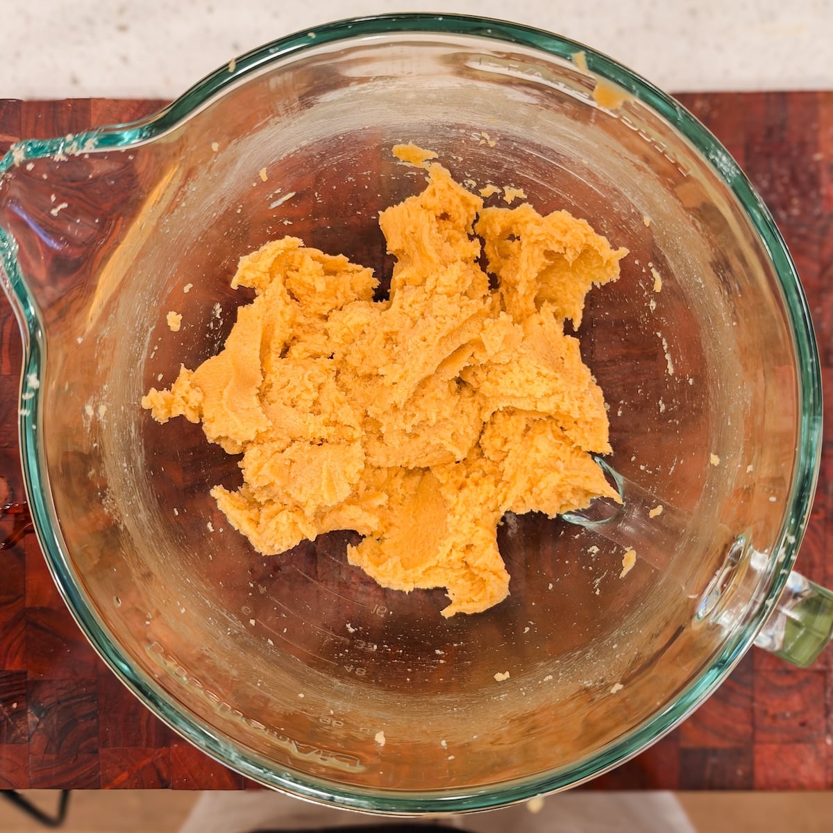 A glass mixing bowl containing a clump of cookie dough being mixed