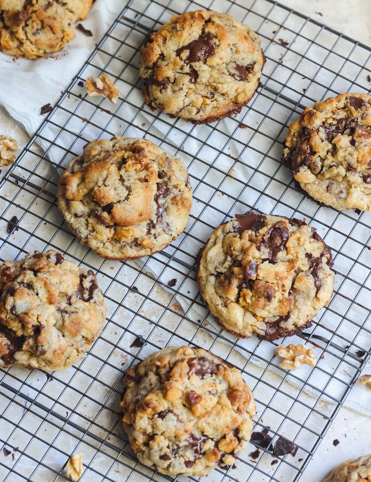 Six levain chocolate chip and walnut cookies on a metal cooling rack. They are golden and crispy outside with some chocolate peeking through