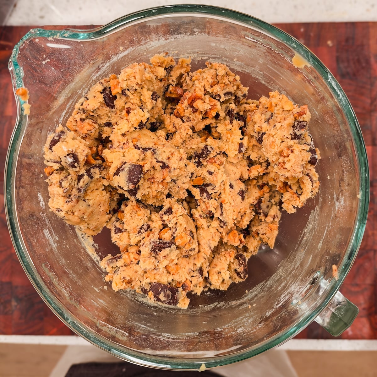 A glass mixing bowl filled with raw cookie dough containing chocolate chips and chopped walnuts.