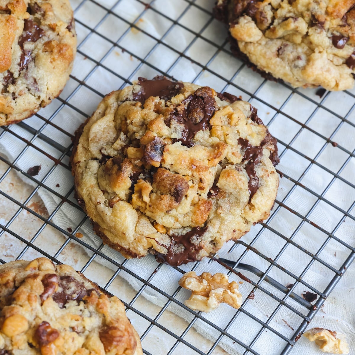 Three chunky, levain style chocolate chip and walnut cookies cooling on a wire rack.