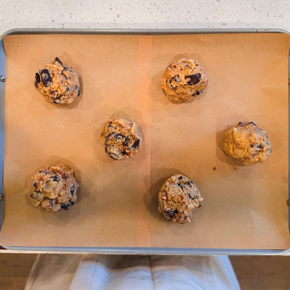 Five balls of chocolate chip walnut cookie dough arranged on a parchment-lined baking sheet.