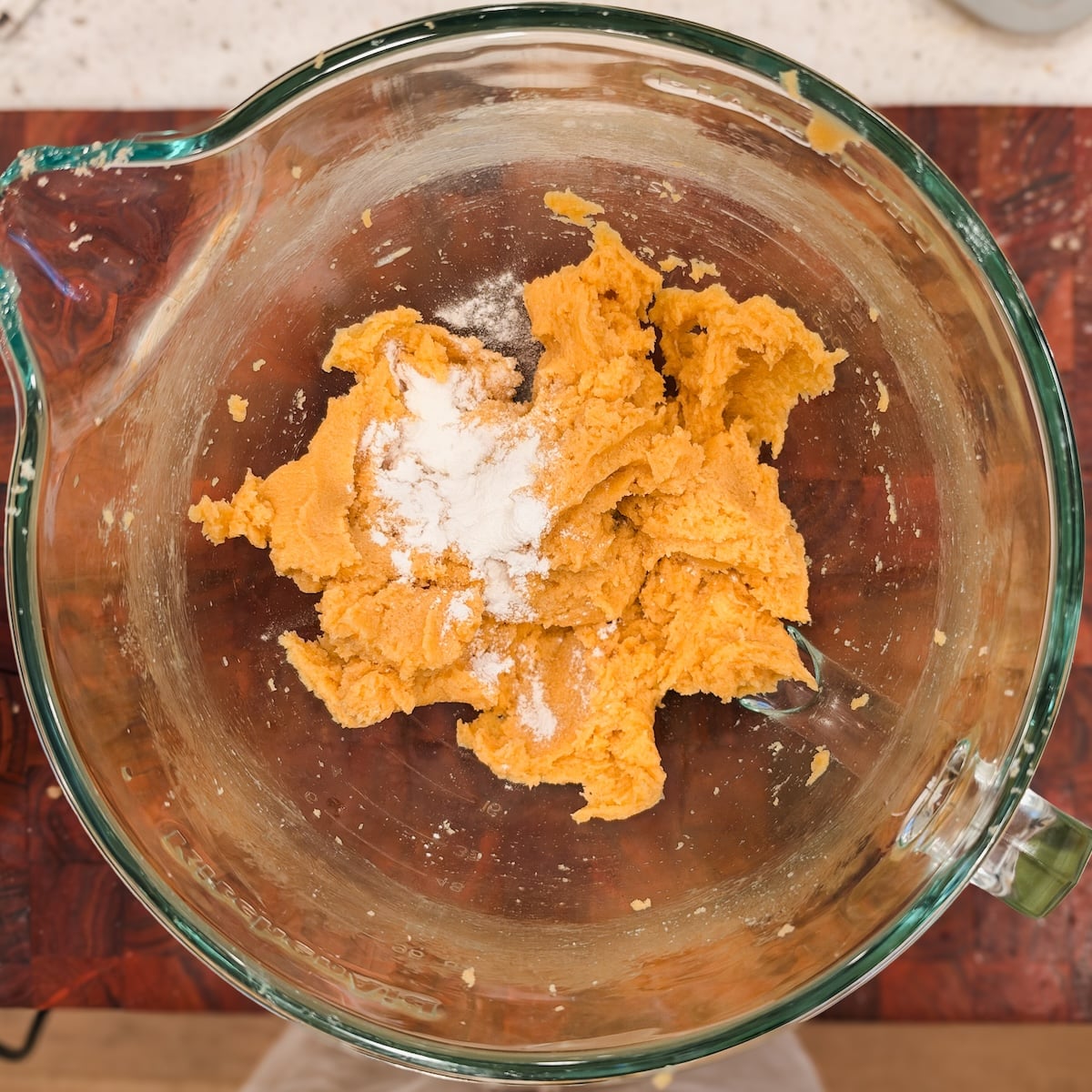 Yellow cookie dough in a glass mixing bowl with a dusting of baking powder and salt on top.